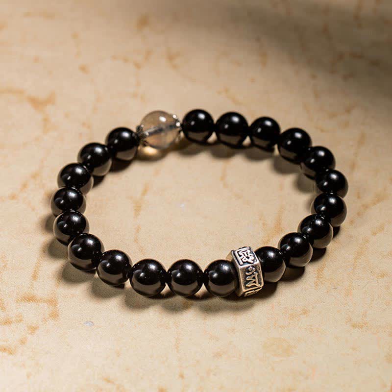 Schwarzes Obsidian Armband mit Silber Charm auf beigem Hintergrund elegant.