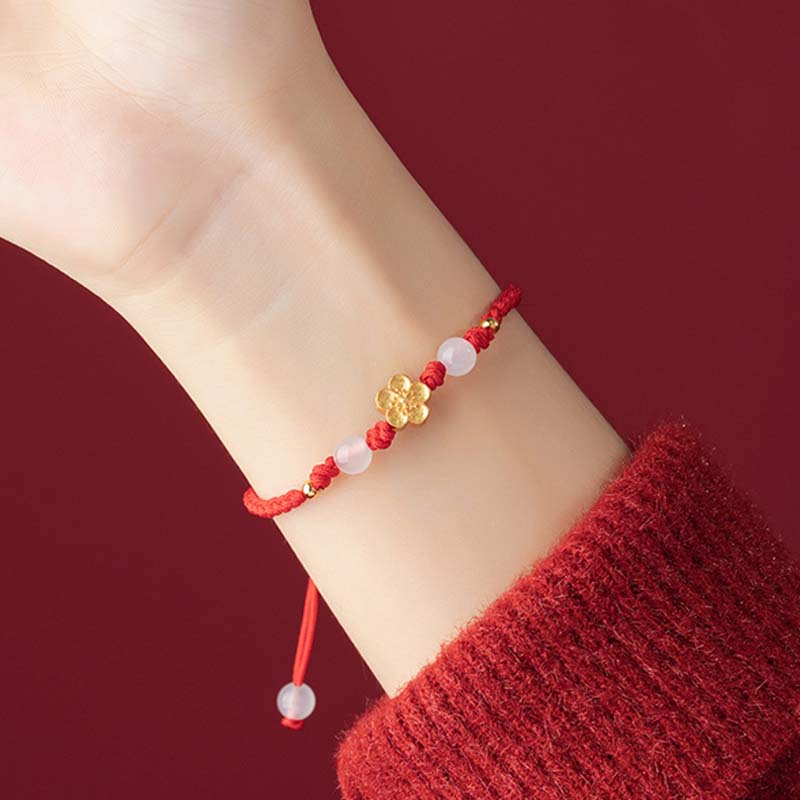 Rotes Armband mit Pfirsichblüte und rosa Steinen am Handgelenk getragen