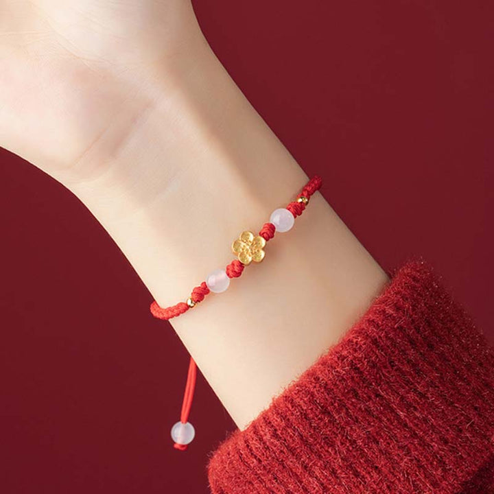 Rotes Armband mit Pfirsichblüte und rosa Steinen am Handgelenk getragen