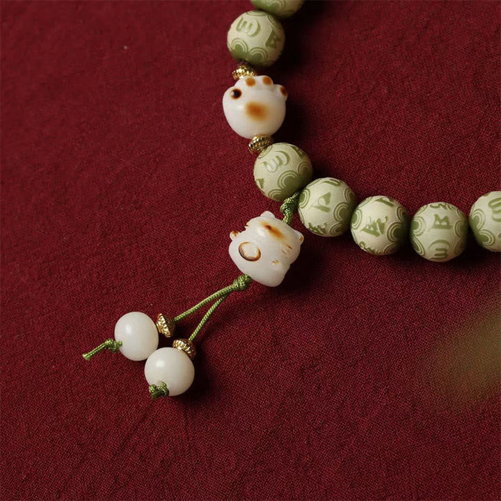 Armband mit weißen Maneki-neko Perlen und grünen Om-Perlen elastisch.
