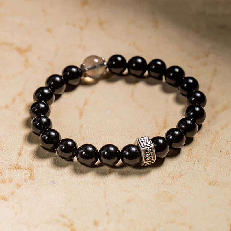 Schwarzer Obsidian Armband mit Silber Charm auf beiger Oberfläche elegant.