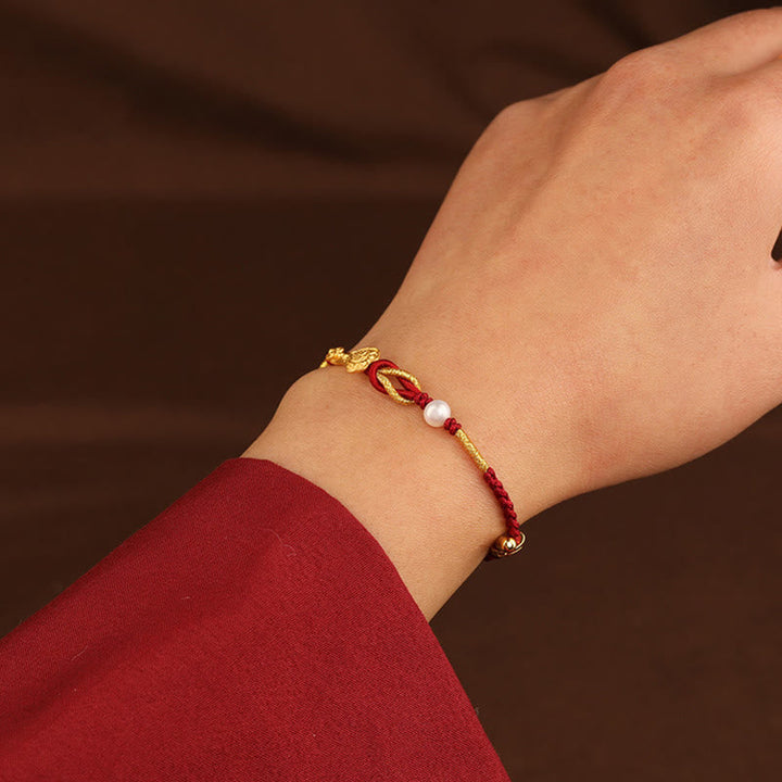 Rotes Armband mit Perle und Fu-Zeichen Glückssymbol am Handgelenk.