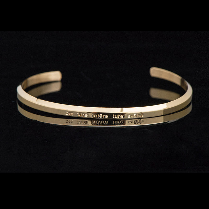 Goldenes Armband mit Gravur auf schwarzem Hintergrund elegant.