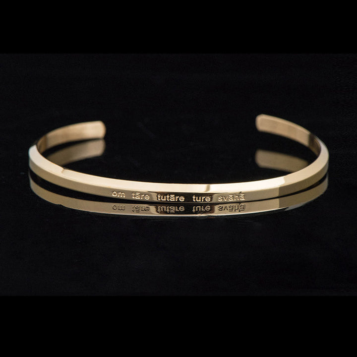 Goldenes Armband mit Gravur auf schwarzem Hintergrund elegant.