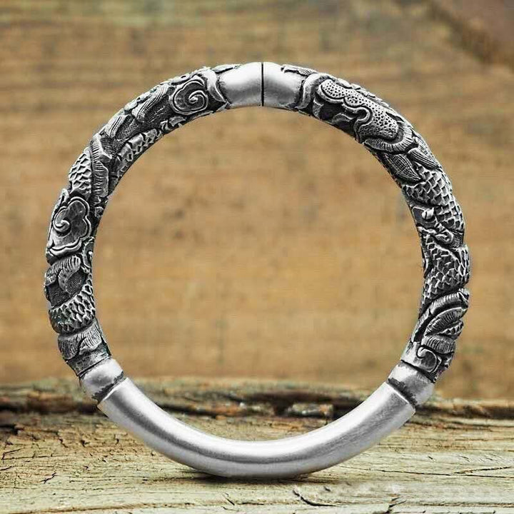 Silbernes Drachen-Armband mit detaillierter Gravur auf Holzuntergrund.