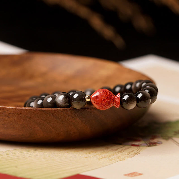 Obsidian Armband mit rotem Koi Fisch Anhänger auf Holzschale.