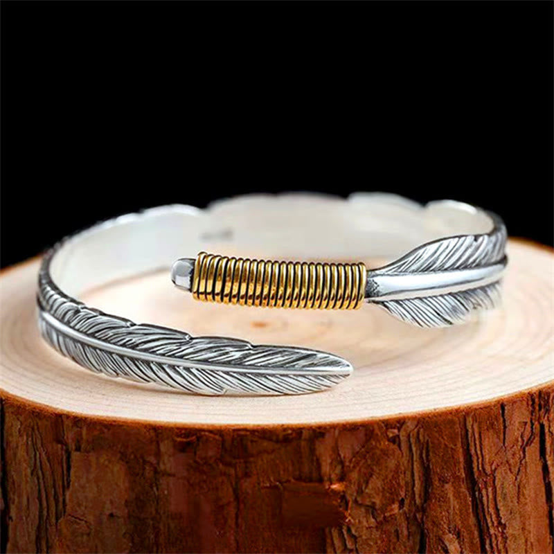 Silbernes Feather Armband mit goldenem Detail auf Holz.