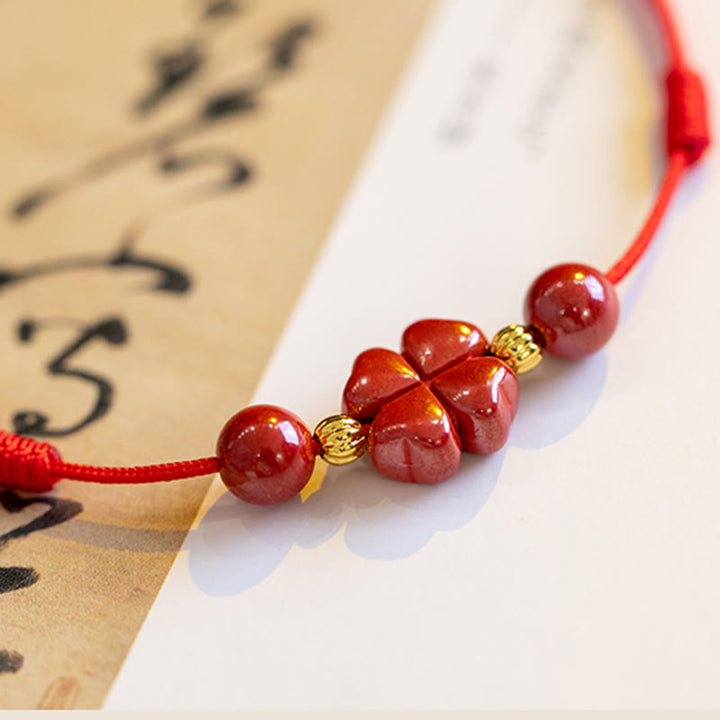Rotes Armband Zinnober Kleeblatt mit Goldelementen auf Papier, Nahaufnahme.