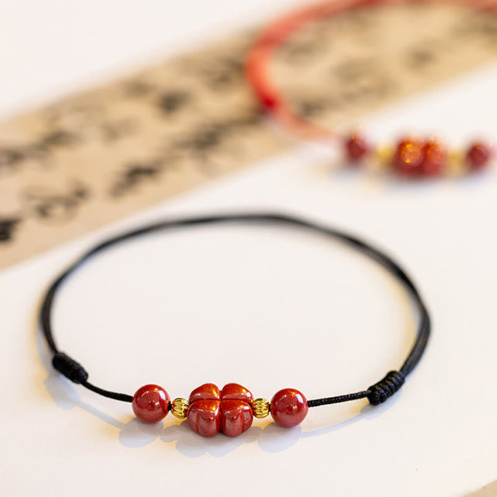 Rotes Zinnober Kleeblatt Armband mit schwarzer Kordel auf weißem Hintergrund Flachlage