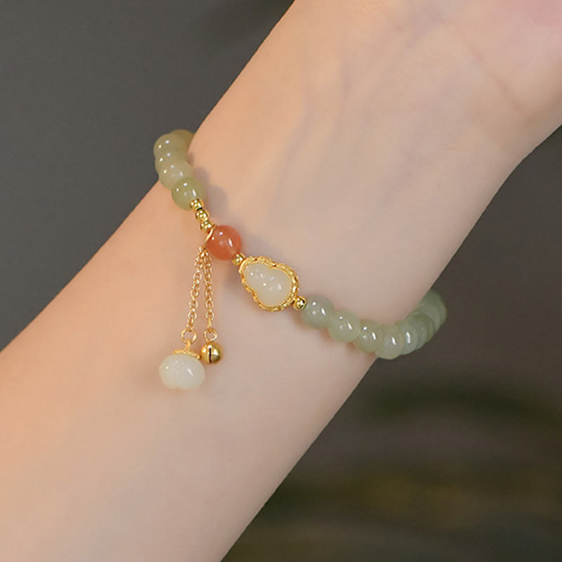 Jade-Armband mit goldenem Lotusanhänger und Quastenverzierung am Handgelenk.