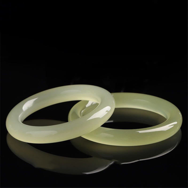 Zwei hellgrüne Jade Armbänder elegant auf schwarzem Hintergrund.