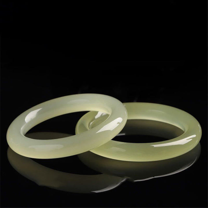 Zwei hellgrüne Jade Armbänder elegant auf schwarzem Hintergrund.