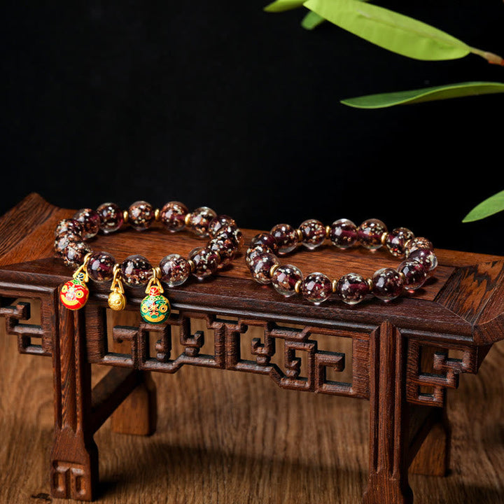 Granat Armband mit goldenen Anhängern auf Holzständer elegant.