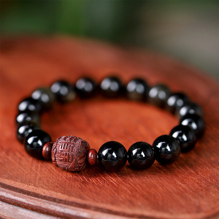 Schwarzes Obsidian Armband mit Om Symbol Perle auf orangefarbenem Stoff.
