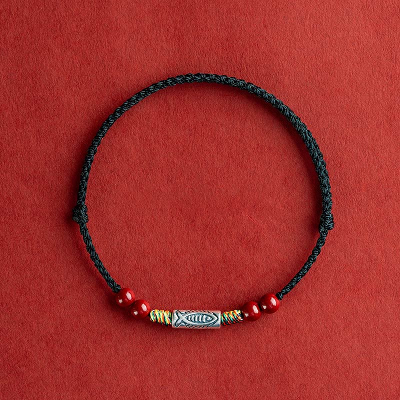 Schwarzes Armband mit roten Perlen und Fisch-Anhänger auf rotem Hintergrund.