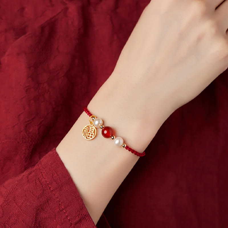 Rotes Armband mit Perlen und goldenem Fu-Zeichen Anhänger.