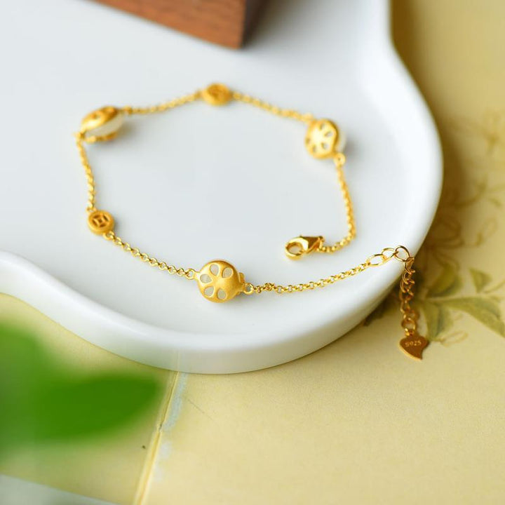 Goldenes Armband mit floralen Charms auf weißer Schale elegantes Design.