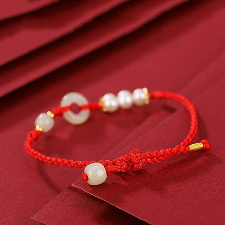 Rotes Armband mit Perlen und goldenem Verschluss elegant präsentiert.