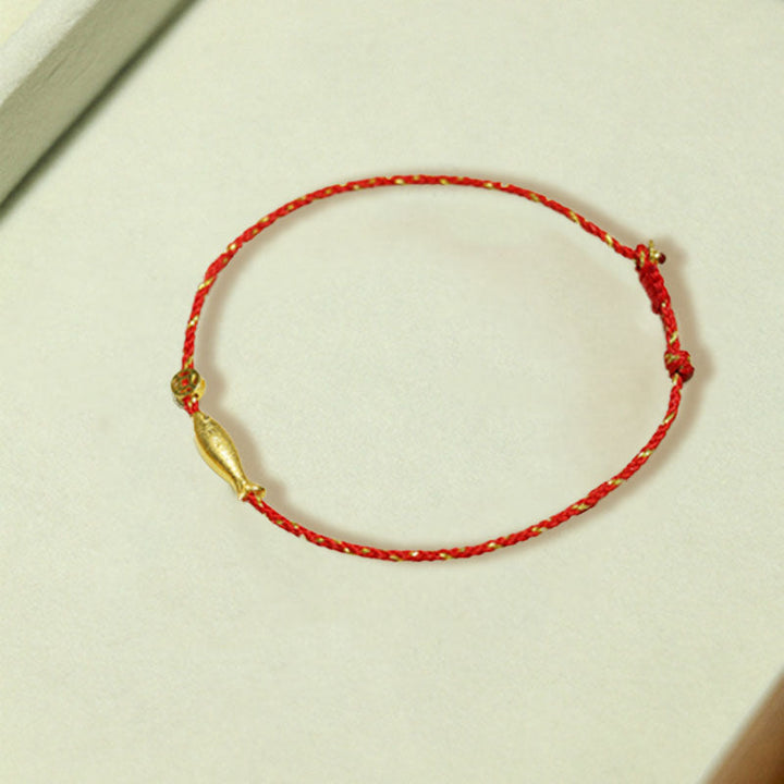 Rotes Armband mit goldenem Koi Fisch Anhänger auf Tisch.