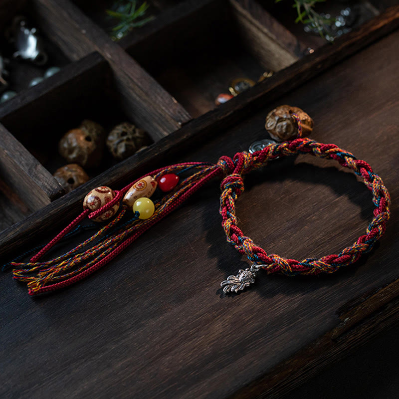 Rotes geflochtenes Armband mit Perlen und Silberanhänger auf Holz.