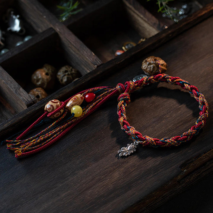 Rotes geflochtenes Armband mit Perlen und Silberanhänger auf Holz.