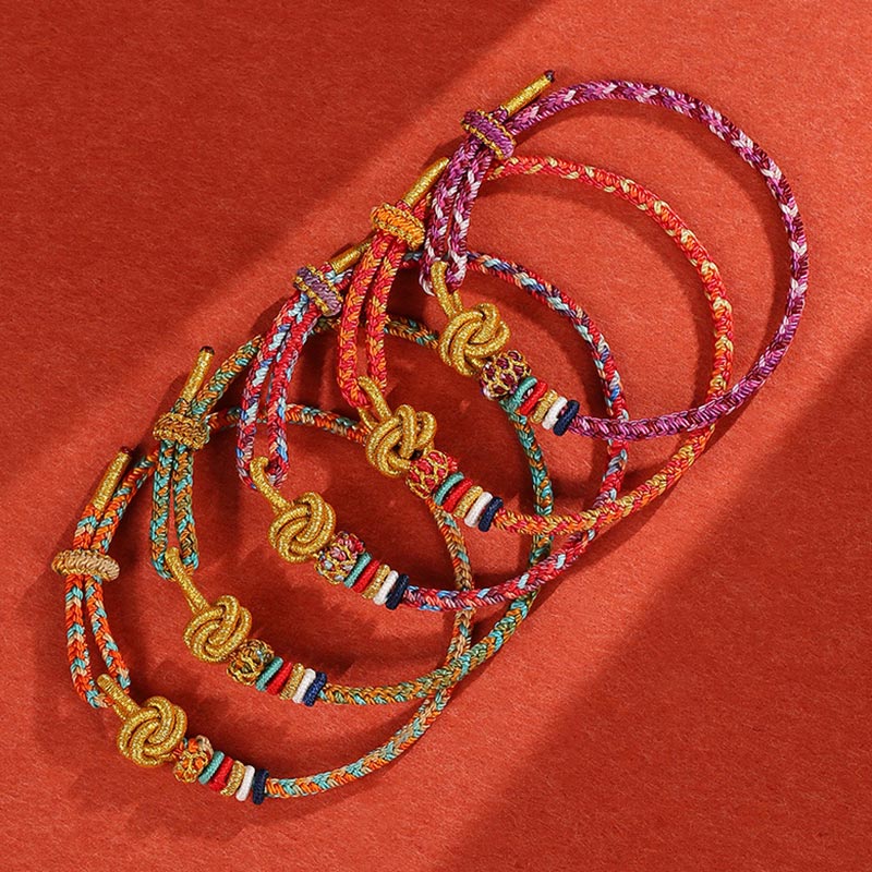 Bunte geflochtene Armbänder mit goldenem Knoten auf rotem Hintergrund