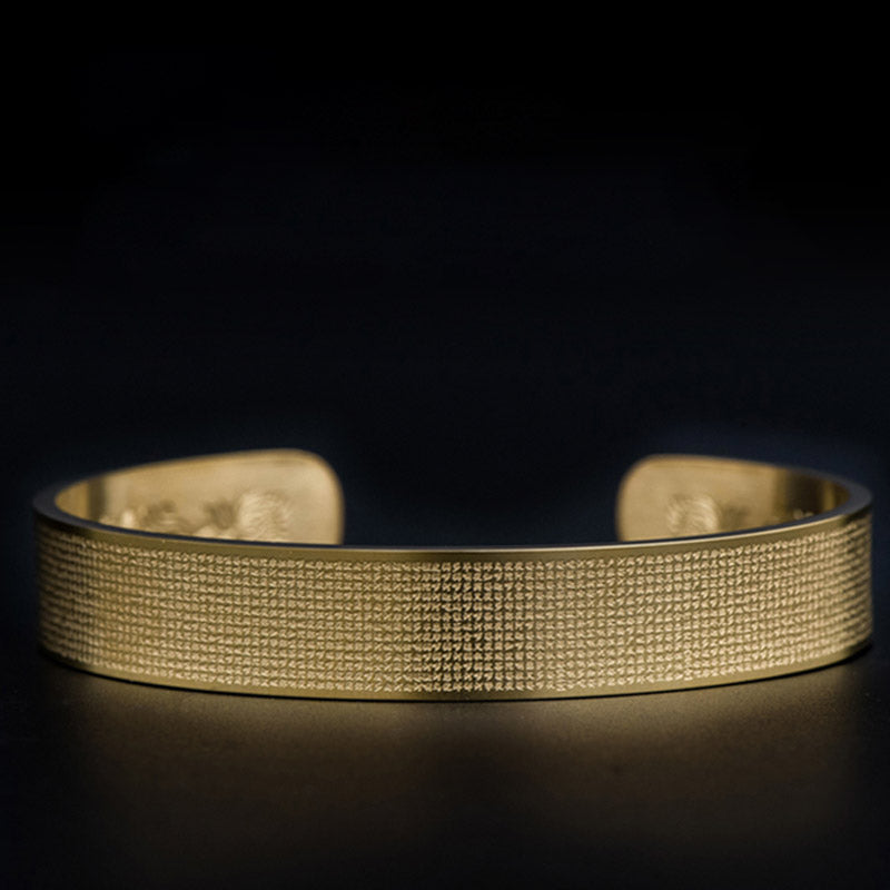 Goldenes Armband mit Gravierung auf schwarzem Hintergrund elegant.
