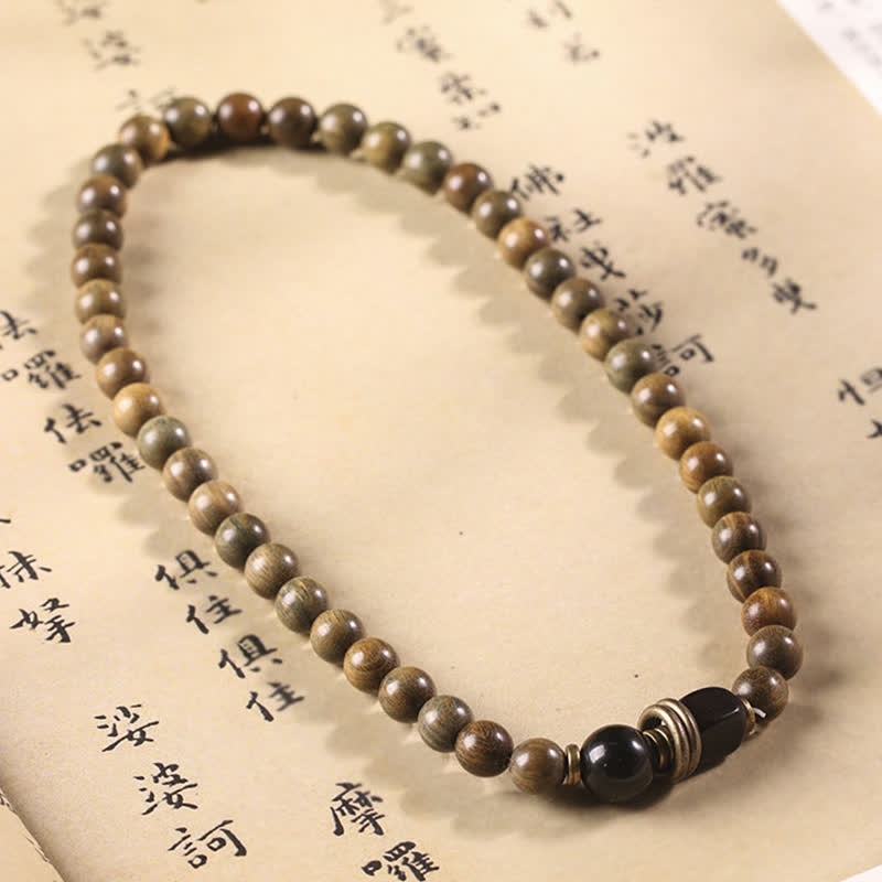 Sandelholz Kristall Armband mit schwarzem Stein auf antiker Schrift.