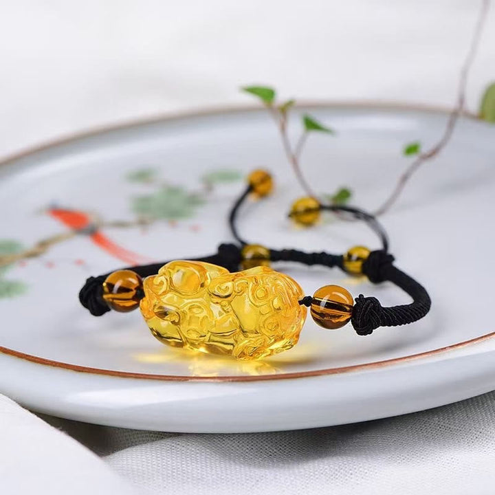 Goldenes Pixiu Armband mit schwarzem Band auf weißer Schale Dekoration.