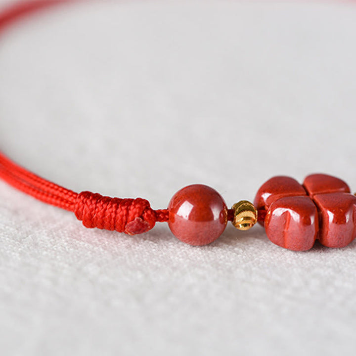 Rotes Armband Zinnober Kleeblatt mit goldenen Perlen auf Textil.