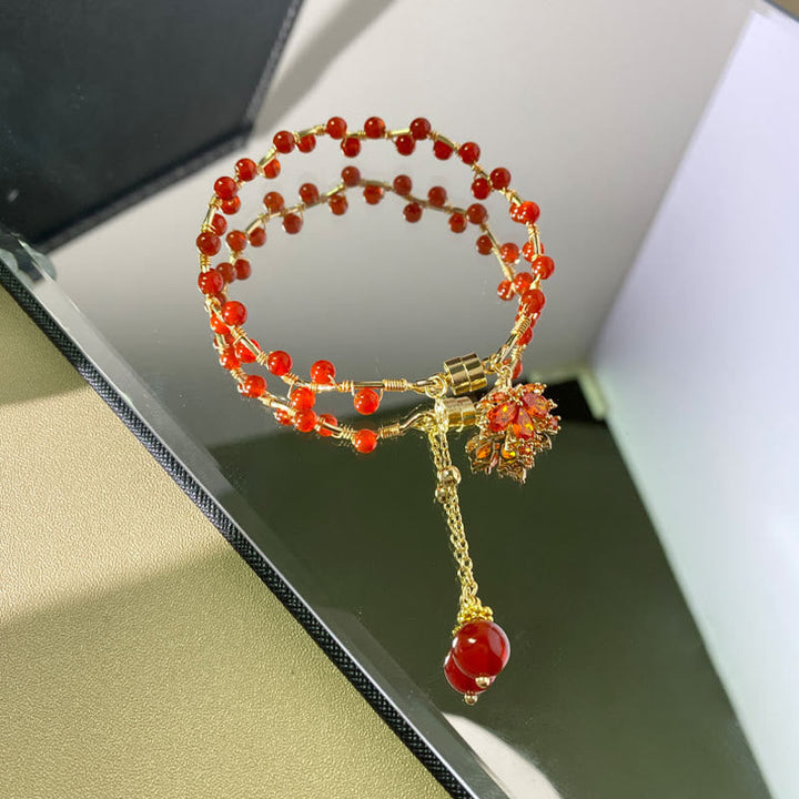 Rotes Armband mit Ahornblatt-Charm und Glücksperlen, elegant.