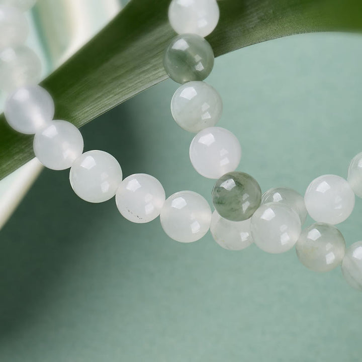Armband Jade Achat Glück Fülle helle Perlen auf grünem Blatt Nahaufnahme