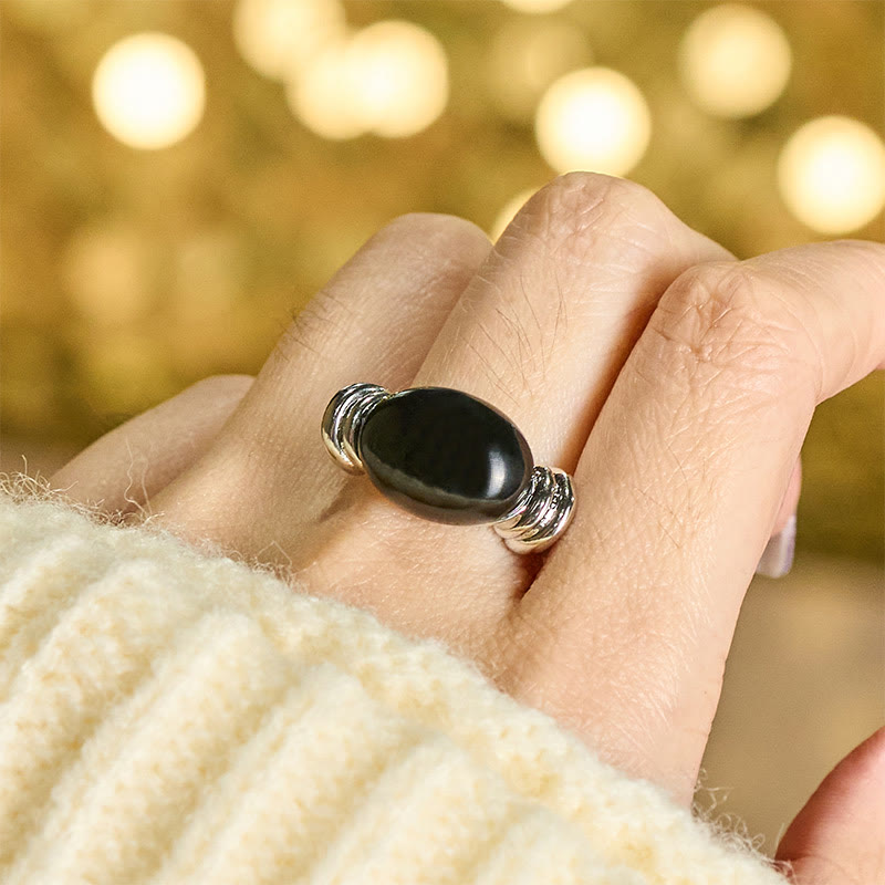 Hämatit Ovalmuster Ring getragen an Finger mit goldenem Bokeh Hintergrund